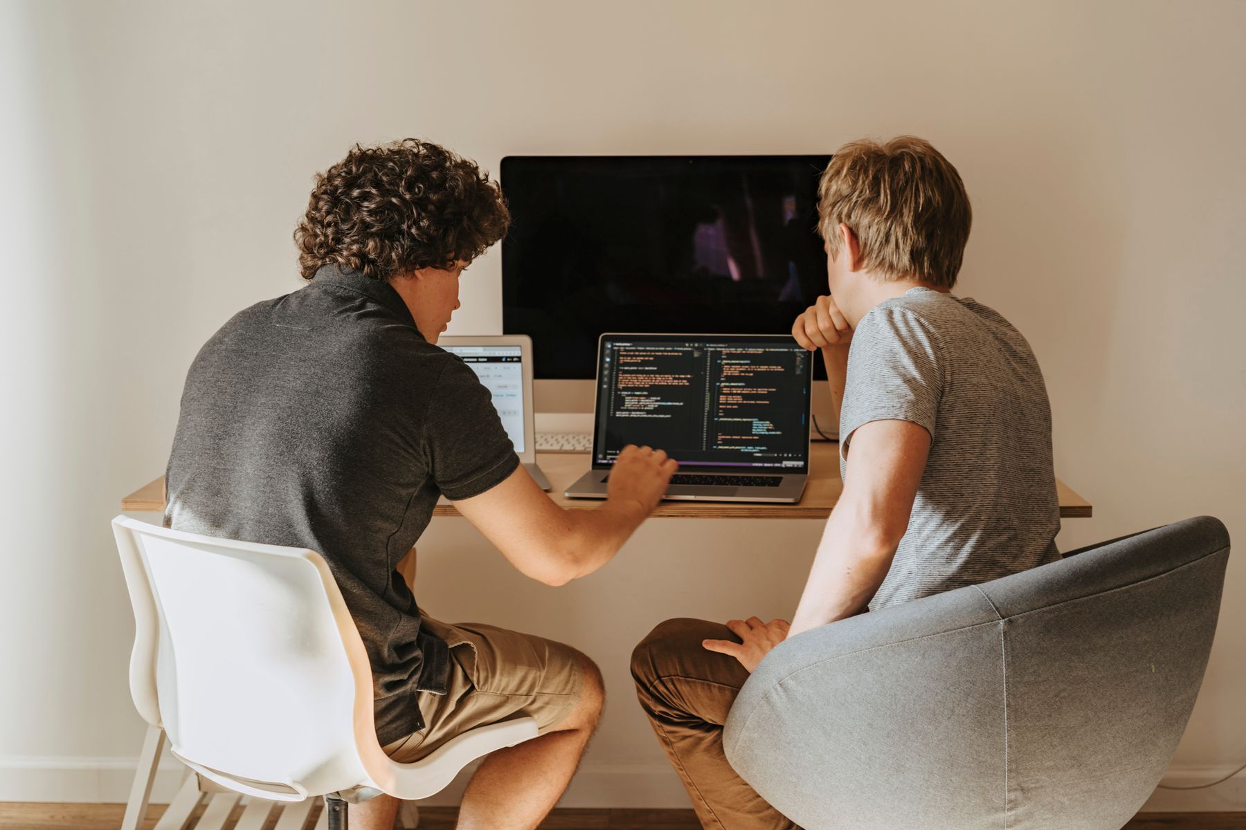 Two developers discuss code on a laptop at a shared desk.